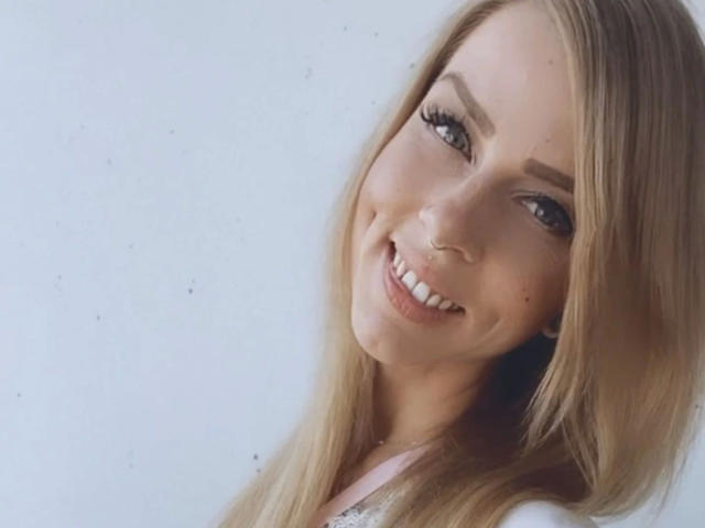PixiFleur-hot has blonde hair, blue eyes, and a nose ring, smiling with white teeth, wearing a pink top, and has long eyelashes and a cute, sexy face.