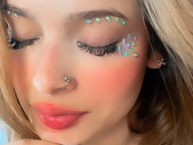 ShantalSummer's face with glitter on her eyelids and cheek, pink blushed skin, red lips, nose ring, long blonde hair, and closed eyes. Her tits are not visible.