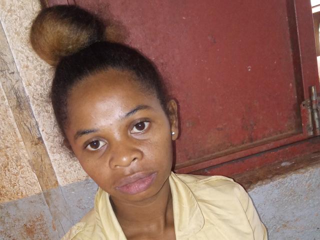 Niri has dark brown skin, small tits, and a bun hairstyle. She's wearing a yellow shirt, looking serious with slightly parted pink lips. Her brown eyes are centered.