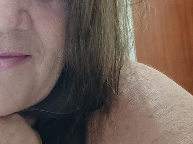 YayaMinera's shoulder with visible skin texture, brownish hair, and partial face showing pink lips. Her hand rests near her chin. The image focuses on her upper body.
