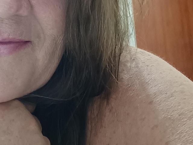 YayaMinera's shoulder with visible skin texture, brown hair, and partial face showing pink lips. Boob partially visible, slightly pressed against her shoulder. Soft, natural light.