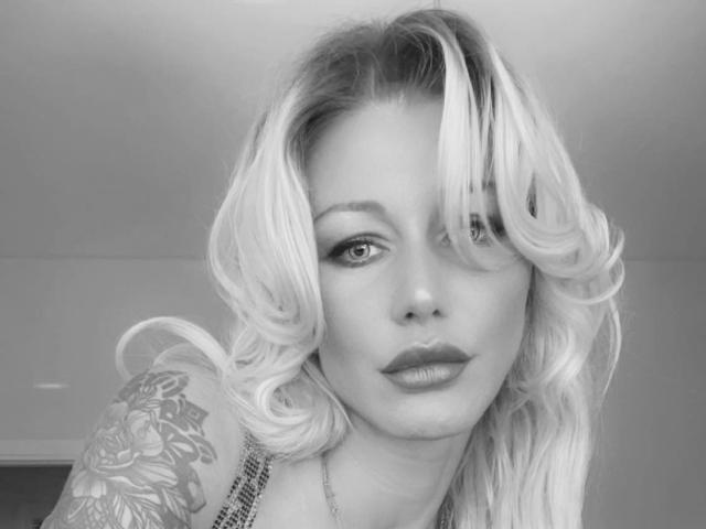 Alisssa has blonde, wavy hair, a tattoo on her right shoulder, and is looking at the camera with pouty lips, wearing a sleeveless top. Black-and-white photo.