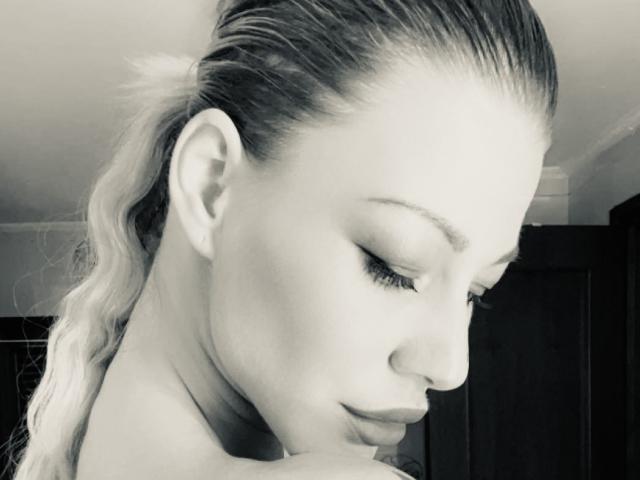 Black-and-white photo of Alisssa with closed eyes, long wavy hair pulled back, subtle makeup, and a slight smile, showing her smooth face and gentle expression. Her tits are not visible.