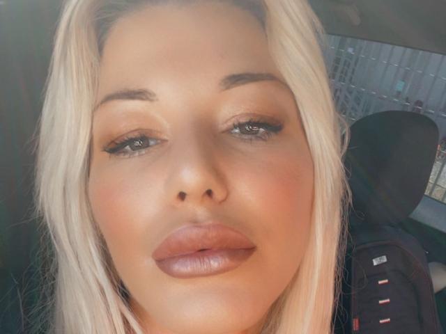 Alisssa has blonde hair, full lips with glossy pink lipstick, and subtle eye makeup, looking directly at the camera with a slightly pouty expression in a car.