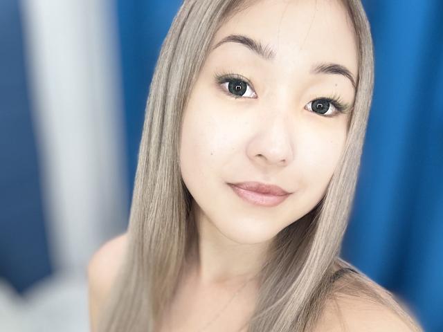 RenyLime has long blonde hair, green eyes, and light pink lips. She's looking at the camera with a slight smile. Her makeup is subtle with long eyelashes.