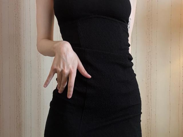 La robe noire, texturée et moulante de Keiri met en valeur sa taille fine et sa main posée sur sa hanche. Ses doigts sont légèrement recourbés, et un petit tatouage est visible sur son côté..