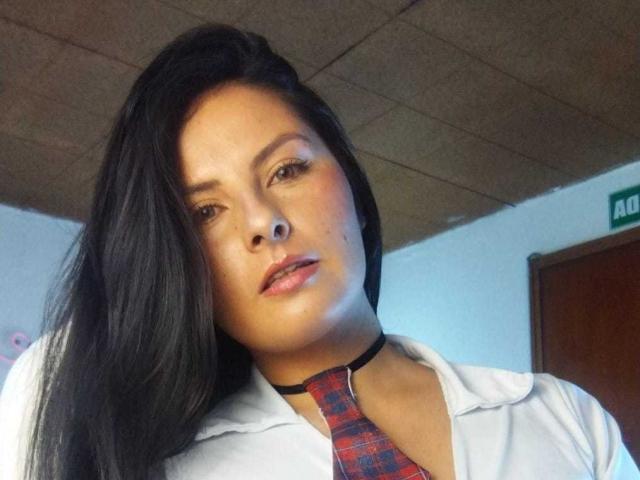 BrandySweet with long black hair, brown eyes, and tan skin, wearing a white shirt and red plaid tie, looking slightly down with a subtle, relaxed expression.