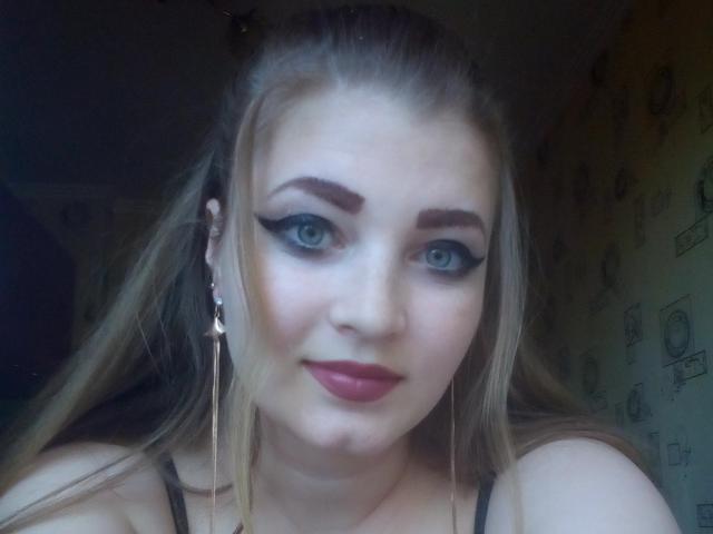 ElizabethHottie has blue eyes, black eyeliner, red lipstick, and long blonde hair. She's wearing a black bra with gold earrings and a subtle smile.