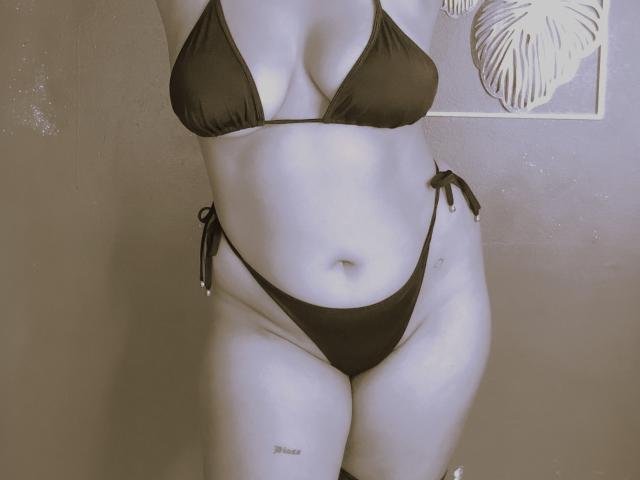 LisCruz in a black bikini, showing her tits in a tiny top and her pussy in high-cut bottoms, with a tattoo on her right thigh.