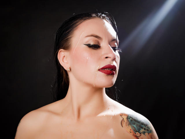 KatalinaJohnson has wet black hair, red lipstick, and a tattoo on her shoulder. She's covered in water, with droplets on her face and chest. Her tits are visible.