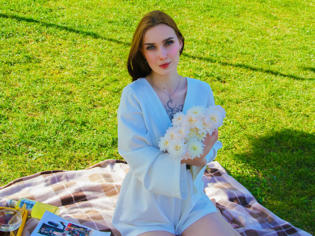 AlexisHott with light brown hair, wearing a white dress, holding a bouquet of white daisies, sitting on a plaid blanket, grassy background, sunny, blue eyes, slight smile.
