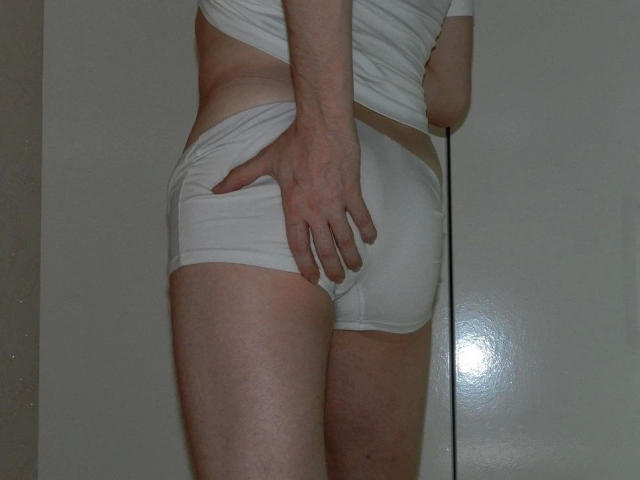 A photo of justfun72-hot with pale skin, wearing white shorts, standing with their back to the camera, hand on their butt, showing a slight tan line.