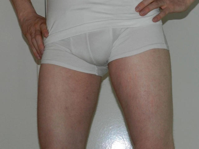 Justfun72-hot's white boxer shorts, showing a slight bulge in the crotch, with hands on their hips, standing against a plain wall, displaying their pale, slightly hairy thighs.