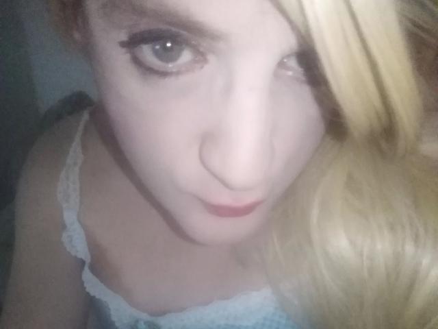 ZackaSissy20-hot has pale skin, blonde hair, and blue eyes, with eyeliner and light pink lipstick, wearing a blue lace bra, looking up with a slightly pouty expression.