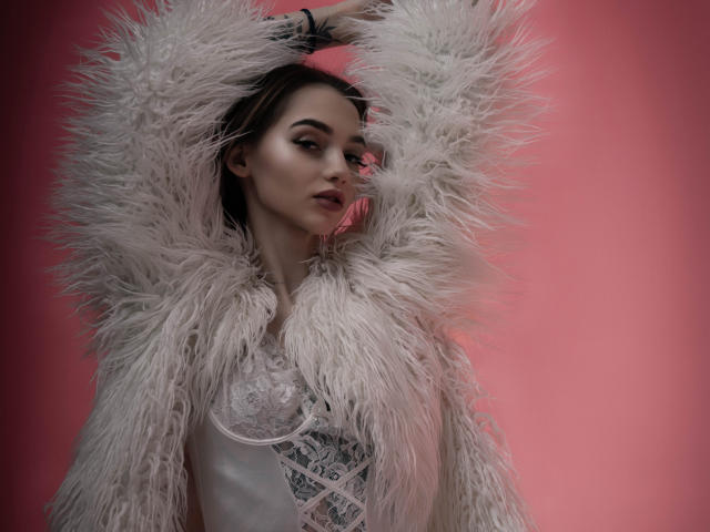 SophieKitty with fluffy white coat, arms raised, serious expression, brown hair, light makeup, lace top, pink background, soft lighting, detailed fur texture, sexy and elegant.