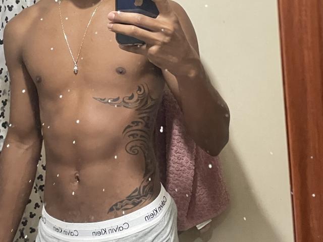 ViiTor's toned, dark-skinned torso with a tribal tattoo on the left side, wearing white Calvin Klein underwear, holding a phone, reflecting in a mirror with speckles.