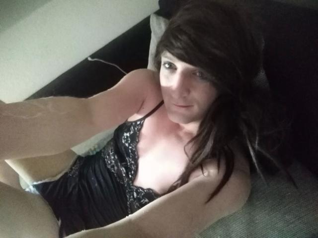 ZackaSissy20-hot with dark hair, pale skin, and lace black camisole, showing small tits and a slight smile, taking a selfie from above.