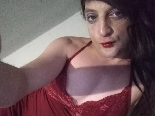 ZackaSissy20 – attraktiv mit langen, schwarzen Haaren, einem roten Spitzenoberteil und rotem Lippenstift, zeigt kleine Brüste und einen hellen Hautton, macht ein Selfie bei schwachem Licht..