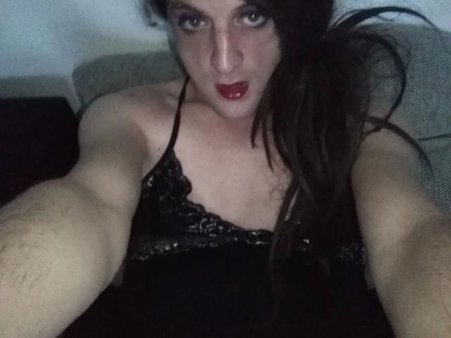 ZackaSissy20-hot with dark hair, red lipstick, and black lace top, showing arms and chest, holding camera, looking up with slightly open mouth, light skin, and small tits.