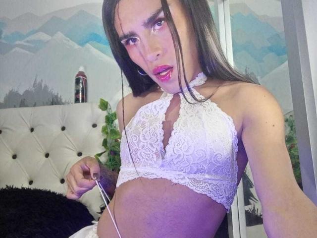Crystalinn with long dark hair, wearing a white lace halter top, showing small tits, holding a wire, pink lipstick, and a bottle on a tufted white headboard.