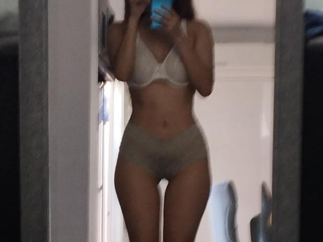 MileyWatson in a mirror selfie wearing a white bra and grey lace panties, holding a blue phone, with visible tits and pussy, standing in a dimly lit room.