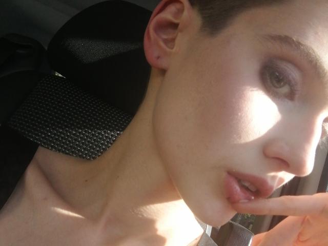 SarahMiss has fair skin, brown eyes, and is biting her finger with her lips slightly parted. She's wearing a black mesh chair and has a small ear piercing.