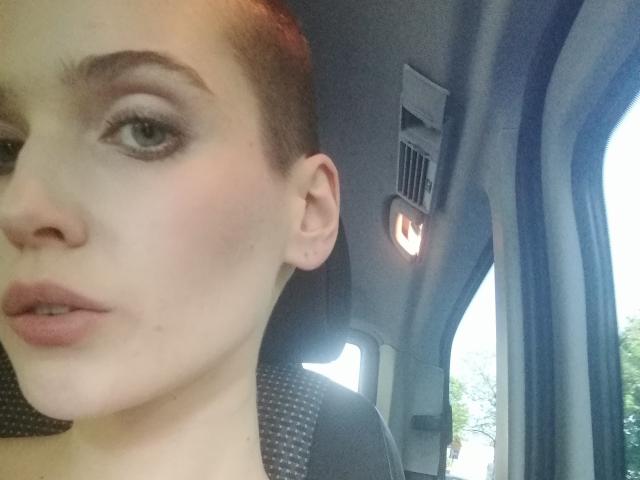 SarahMiss has pale skin, green eyes, and brown hair in a bun. She's pouting with slightly parted lips, wearing subtle makeup, and has a small earring in her ear.