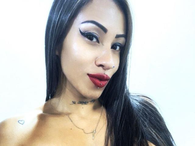 LunaCandy tiene el pelo largo y negro, lápiz labial rojo, cejas pobladas, un piercing en la nariz y un piercing en el labio. Lleva un collar y tiene tatuajes en el cuello y el hombro..