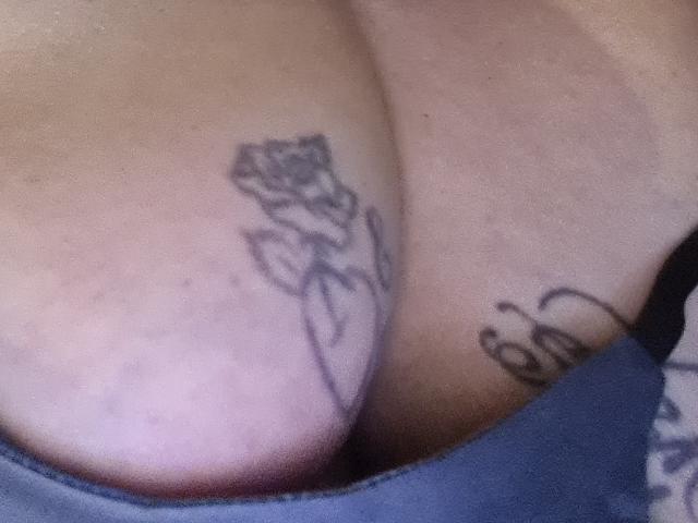 LatexShantie's tits have a rose tattoo on the left and a cursive tattoo on the right, visible in a blurry, close-up shot.