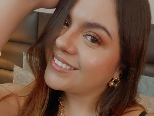 MissSofiia a les yeux marron, un sourire charmant et un petit nez, avec le bras levé. Elle porte des boucles d'oreilles dorées et a une peau claire et brillante..