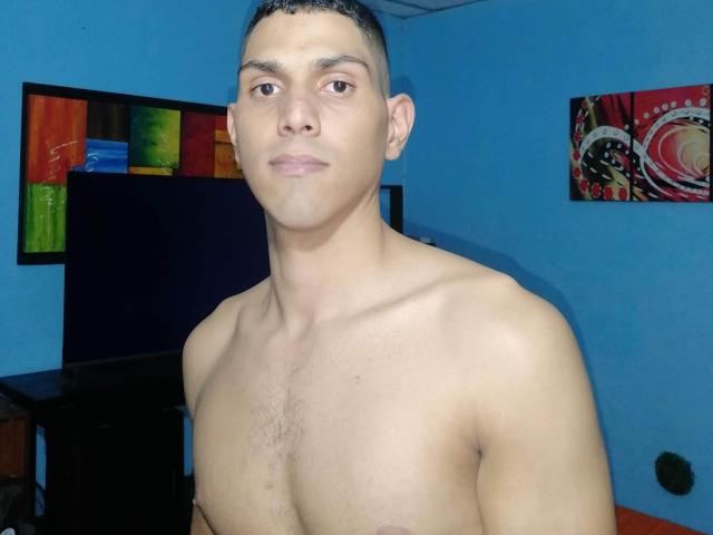 McBride, shirtless with light brown skin, short dark hair, and a slight mustache, has a lean chest with small nipples and a neutral expression.