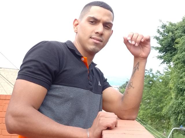 McBride, a muscular dude with a tan skin tone, short black hair, and a tattoo on his right forearm, wearing a black and gray polo, holds his fist up.