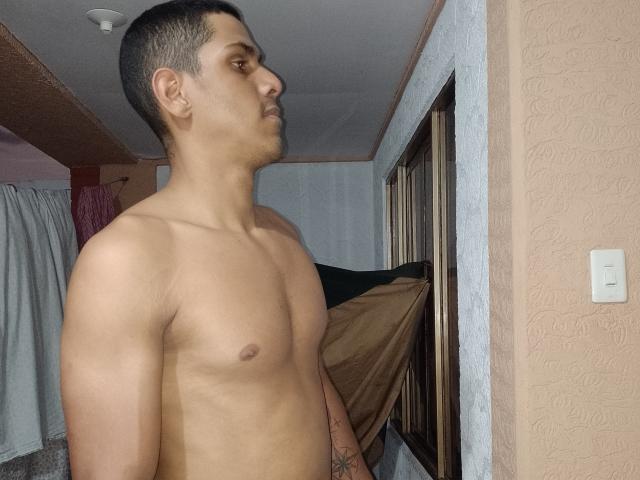 McBride's shirtless, muscular, tan-skinned body with small, dark nipples, short dark hair, and a tattoo on his right forearm, standing in profile, looking to the side.