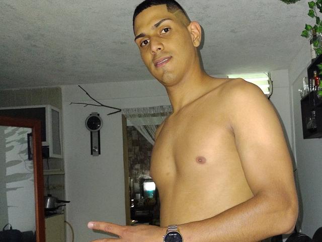 McBride, shirtless with a medium brown skin tone, short black hair, small nipples, and a slight smile, pointing with his right hand, wearing a black wristwatch.