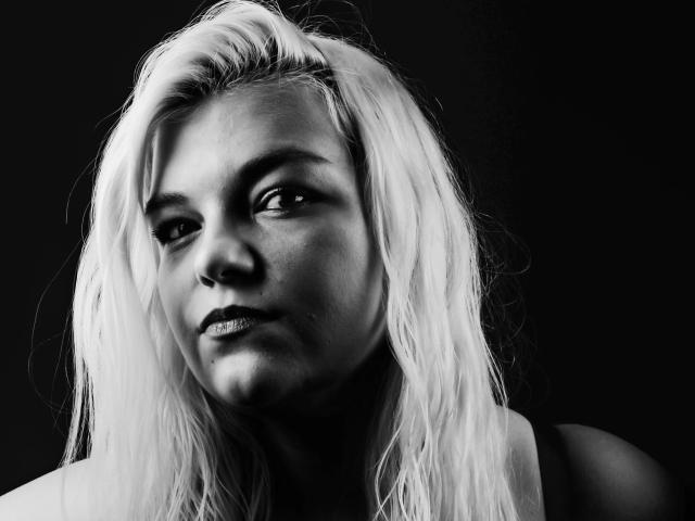 Black-and-white photo of MariellaSun-hot with platinum blonde, wet-looking hair, slight smile, and visible freckles, wearing a sleeveless top, looking to the side with a subtle, confident gaze.