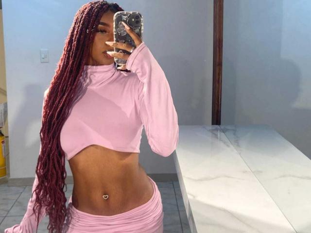 MlleTyra with long red braids, pink long-sleeve crop top, pink pants, showing her toned belly with a navel piercing, taking a mirror selfie.