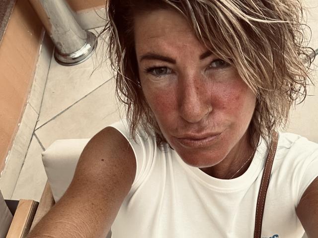 BlackAngeel has red, slightly puffy cheeks, messy blonde hair, and a pouty expression, wearing a white sleeveless shirt with a brown strap, in a tight selfie.