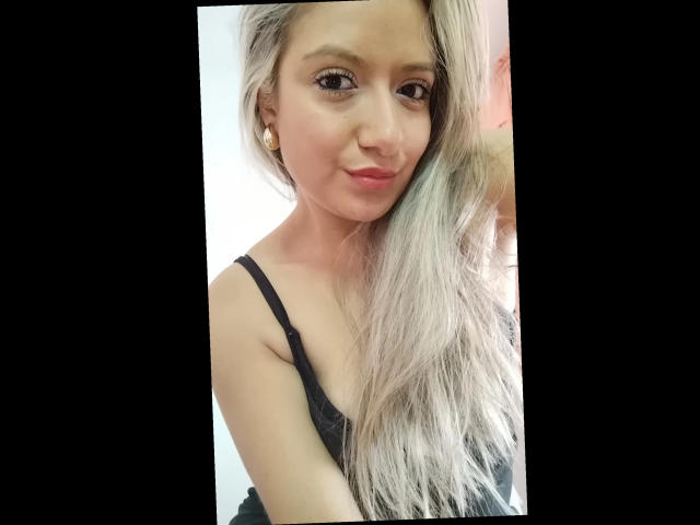 ValeriaHunter69 has long, silver hair, light skin, small tits, wearing a black lace top, with a cute smile and red lipstick, looking at the camera.