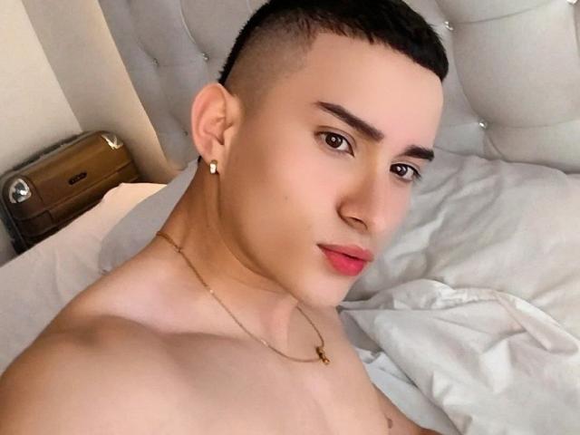 SantiagoXoxo has a cute, smooth face with short black hair, brown eyes, and red lips. He's shirtless, wearing a gold necklace, and a small earring in his right ear.