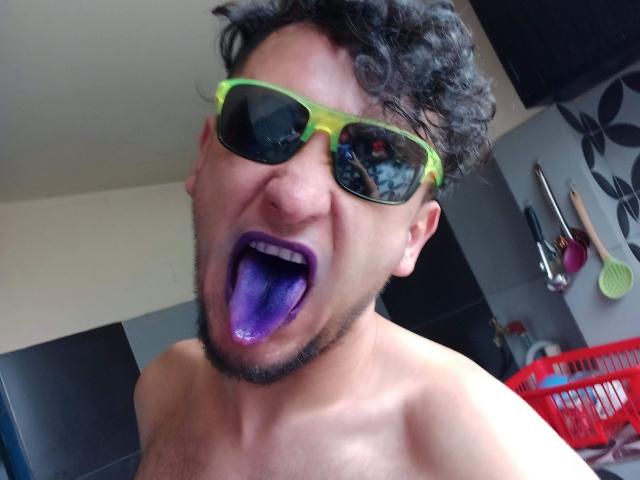 Davydwolf-hot with curly hair, neon green sunglasses, and purple tongue, shirtless, showing a goofy face. Boobs are not visible, but a red laundry basket is in the background.
