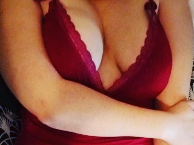 Rose69x's tits in a deep red lace bra, showing ample cleavage with her arms crossed over her chest. Her skin is light, and the bra has a scalloped edge.