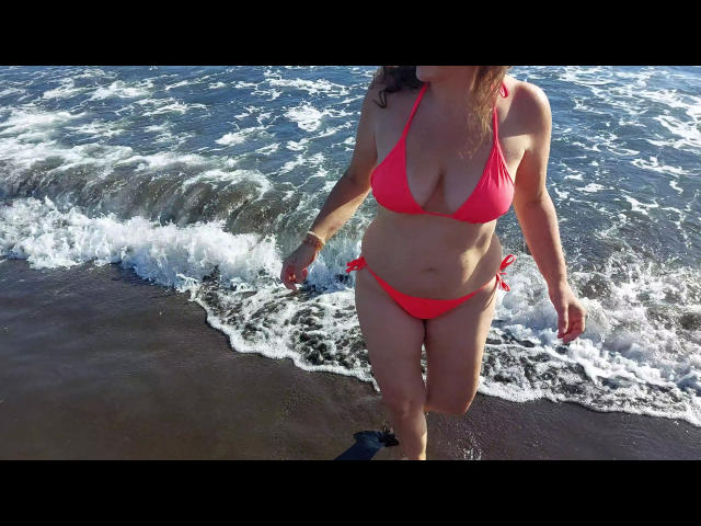 DonJuanundEva-hot with red bikini, showing her tits and ass, walking in shallow ocean water, her face out of frame, wearing a bracelet, and a black sock on one foot.