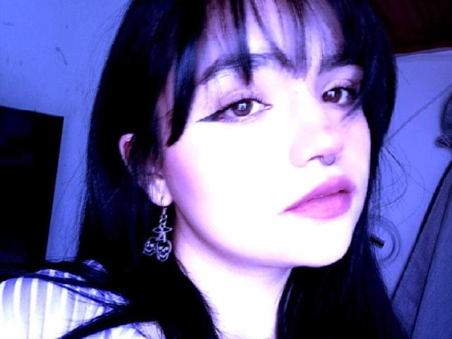 LovelyLilith has dark hair, winged eyeliner, pink lips, a nose ring, and ornate earrings, with a blue-tinted face in the selfie. Her ass is not visible.
