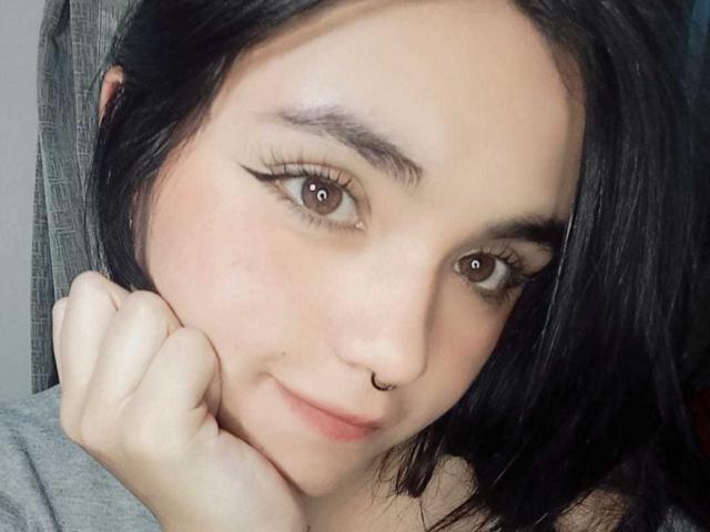 LovelyLilith with black hair, brown eyes, winged eyeliner, nose ring, and a slight smile, resting her chin on her hand, looking cute and sexy.