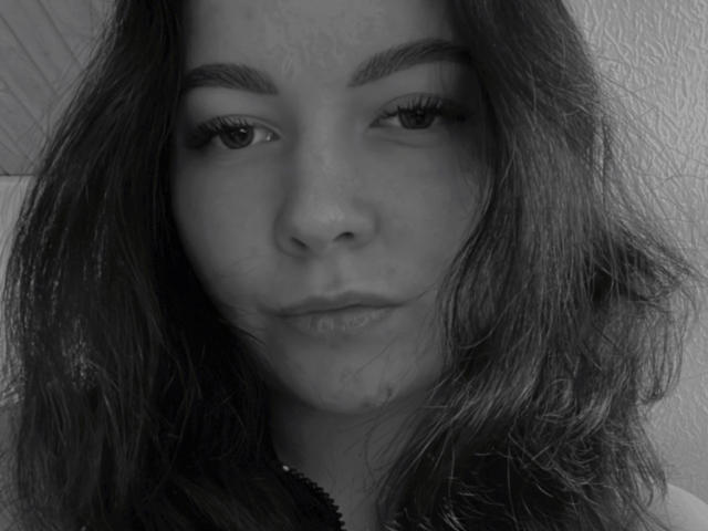 Black-and-white selfie of CutieLina with wavy dark hair, thick eyebrows, long eyelashes, and slightly parted lips showing a subtle pout. CutieLina's nose is centered, looking directly at camera.