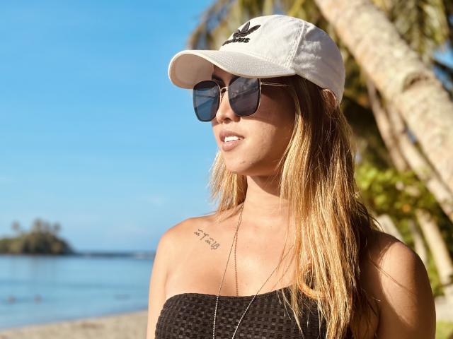 BombshellPh with blonde hair, wearing a white Adidas cap, black textured tube top, and dark sunglasses, has a tattoo on her right chest. Her ass is not visible.