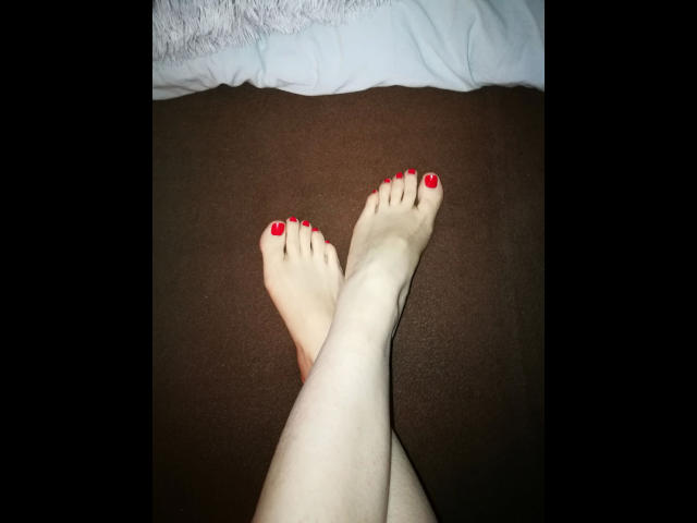 RedJeann-hot's bleke benen, met rode nagellak, waren gekruist op een bruin tapijt, waarbij haar glanzende, goed verzorgde voeten te zien waren..