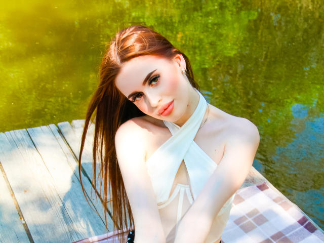 CherylFoxy with long brown hair, white halter top, sitting on a wooden dock, green water reflection, plaid blanket, subtle smile, slightly tilted head, natural light, soft makeup.