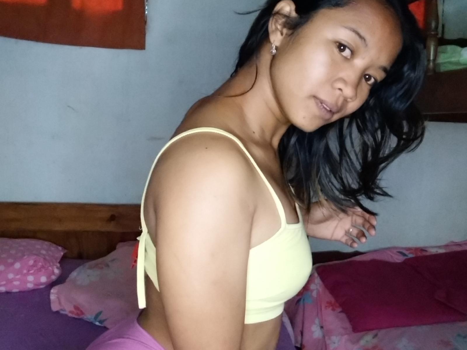 Merten ha la pelle marrone scuro, i capelli neri e ondulati, un reggiseno giallo piccolo e dei pantaloni rosa. Guarda oltre la spalla con un leggero sorriso, mostrando i suoi piccoli seni e i suoi glutei slanciati..