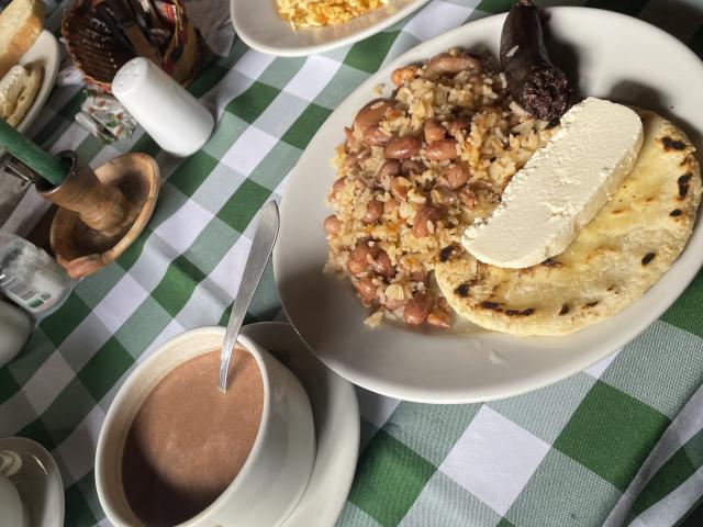 MissSofiia's plate has fried beans, rice, a chunk of cheese, and tortilla, with a cup of brown coffee. Also, some dark chocolate and a white egg.